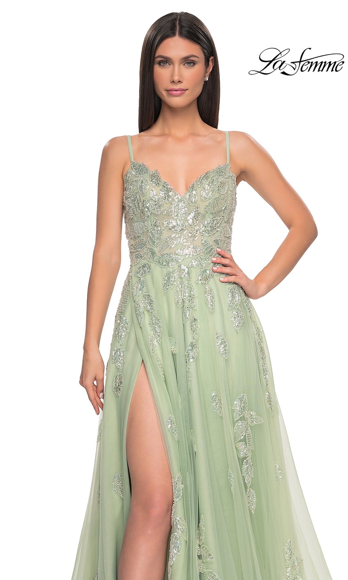 A woman in a sleeveless, light green La Femme Sequin-Embroidered Long Prom Dress 32090 with a thigh-high slit stands with one hand on her hip; the La Femme logo appears in the top right corner.
